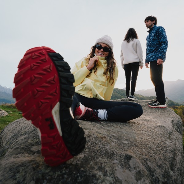 Three friends outdoors on a rocky hilltop with mountains in the background.